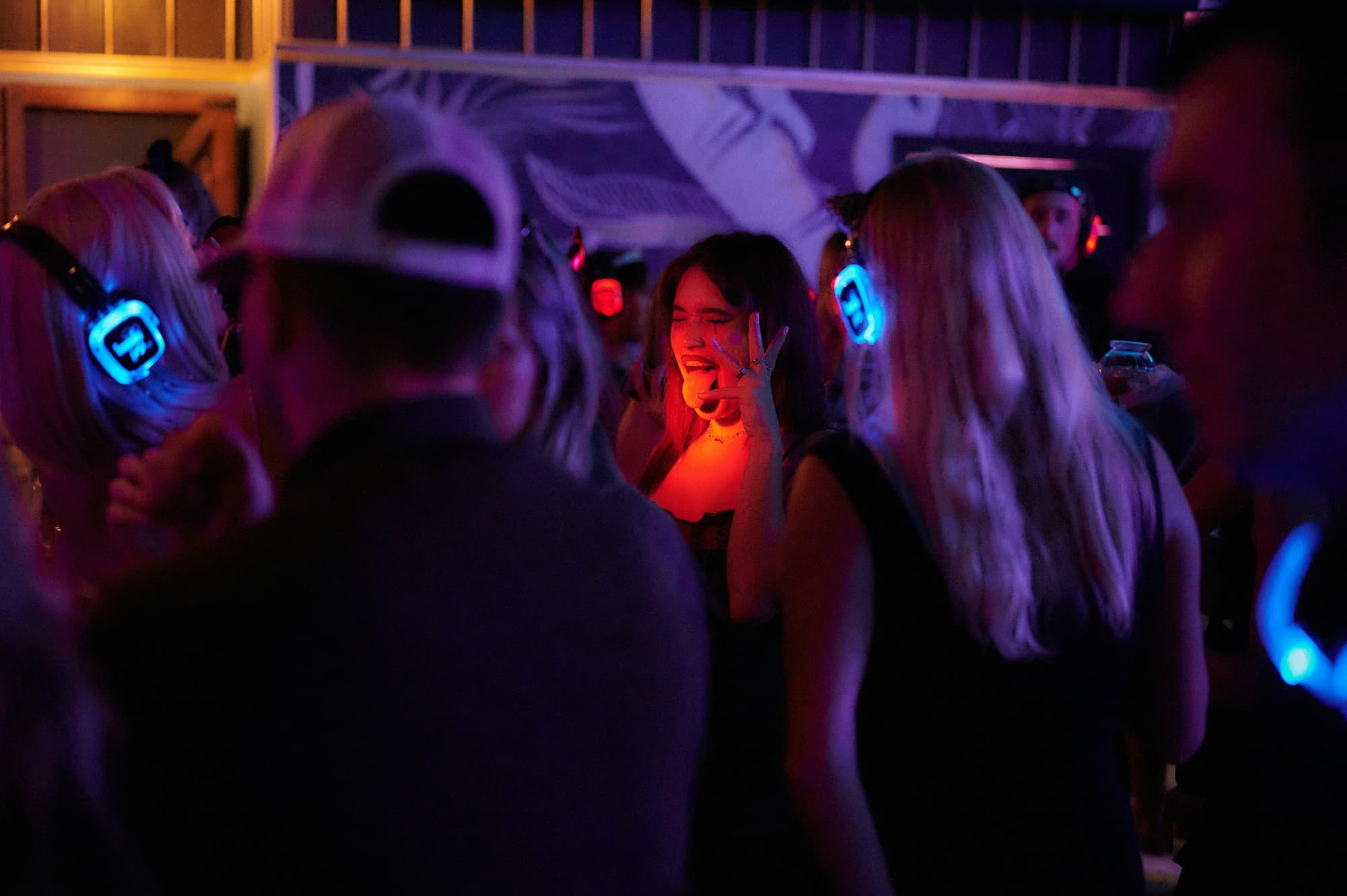 A silent disco dancefloor at night, guests in blue and red lit headphones singing along